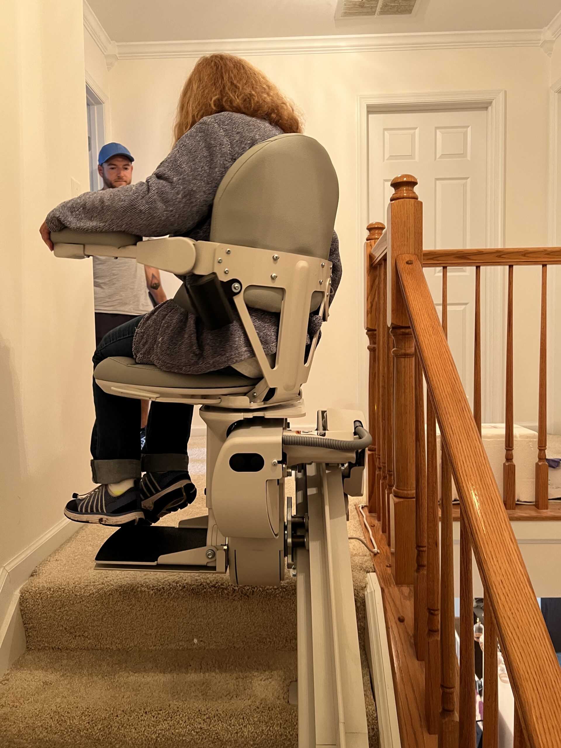 Stairlift repair tech watching woman in Springfield, VA, ride the fixed stairlift up the stairs